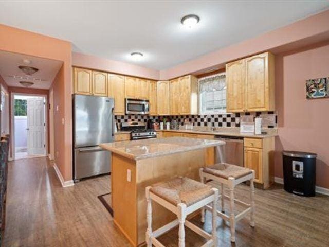 kitchen featuring a breakfast bar area, light brown cabinets, a kitchen island, stainless steel appliances, and decorative backsplash