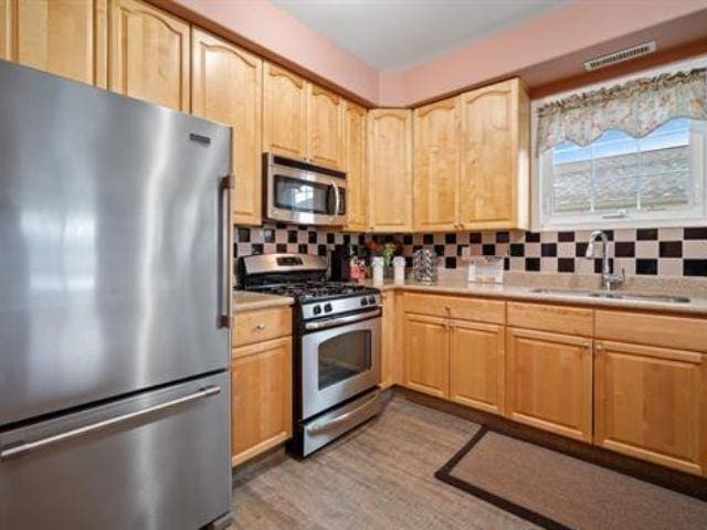 kitchen with appliances with stainless steel finishes, sink, decorative backsplash, and light wood-type flooring