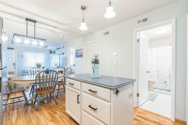 kitchen with light wood-style flooring, white cabinetry, a kitchen island, and decorative light fixtures