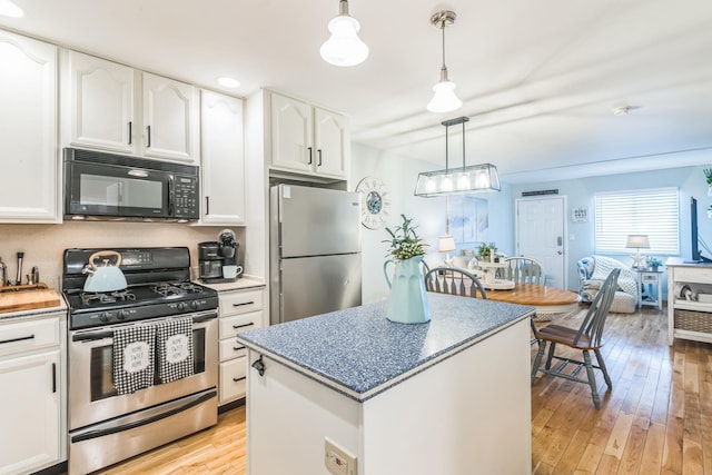 kitchen featuring appliances with stainless steel finishes, light wood-type flooring, white cabinetry, pendant lighting, and a kitchen island