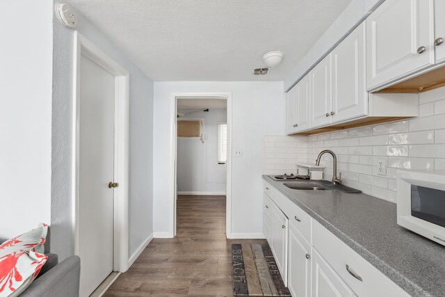 kitchen with white microwave, decorative backsplash, dark wood-style floors, white cabinetry, and a sink