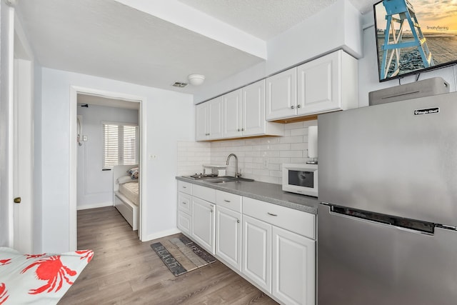 kitchen with white microwave, light wood finished floors, freestanding refrigerator, a sink, and backsplash