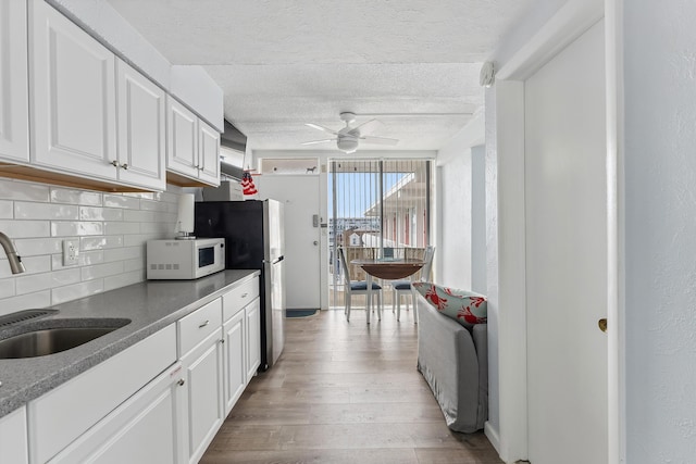 kitchen featuring light wood-type flooring, a sink, white cabinetry, decorative backsplash, and white microwave