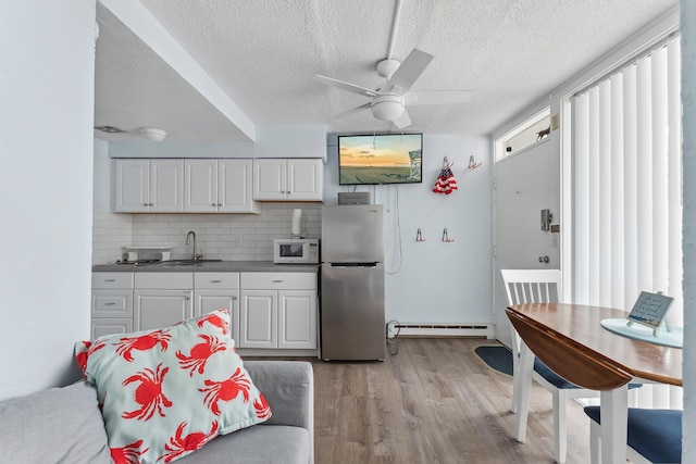 kitchen with a sink, backsplash, freestanding refrigerator, light wood-style floors, and white microwave