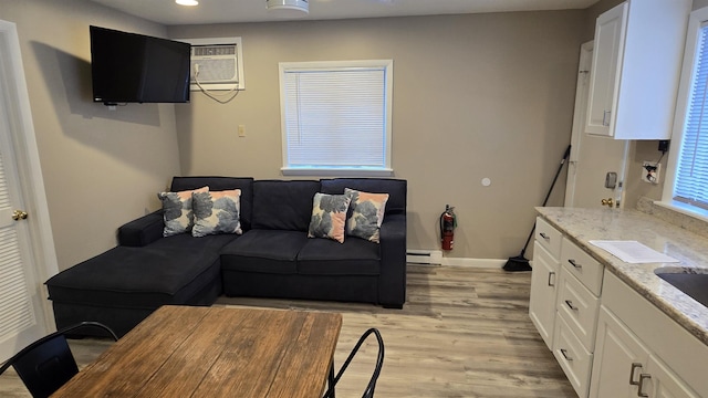 living room with a baseboard heating unit, a wall mounted air conditioner, and light hardwood / wood-style flooring