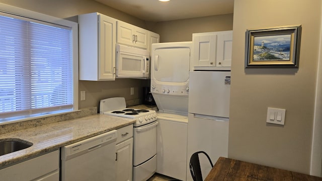 kitchen with white cabinetry, light stone countertops, stacked washer / drying machine, and white appliances