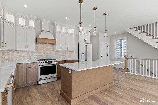 kitchen with high end white refrigerator, gas range, light wood-style flooring, and custom exhaust hood