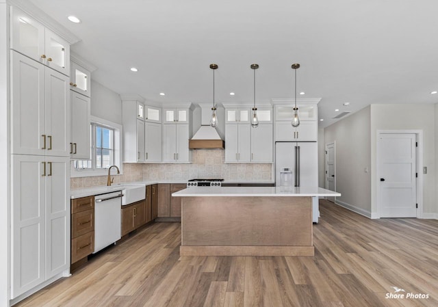 kitchen with white appliances, a sink, a kitchen island, custom exhaust hood, and backsplash