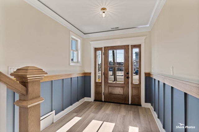 foyer entrance with light wood-style floors, wainscoting, and crown molding