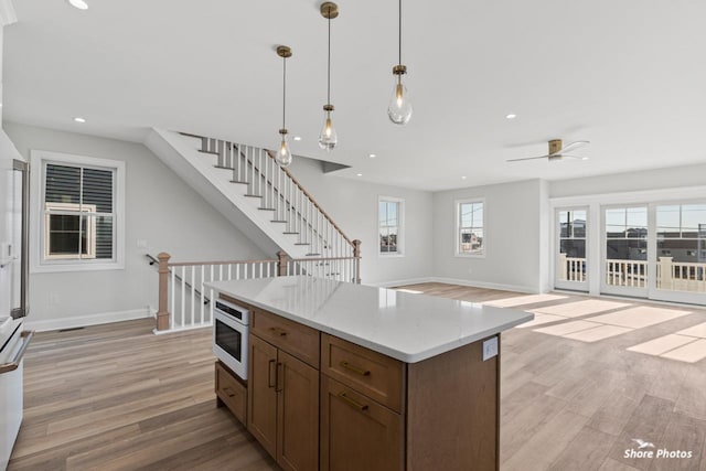 kitchen with built in microwave, hanging light fixtures, open floor plan, light wood-type flooring, and baseboards