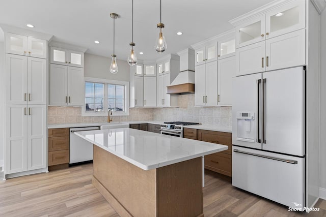 kitchen featuring premium appliances, tasteful backsplash, light wood-style flooring, a sink, and premium range hood