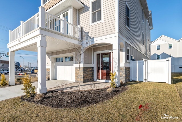 view of front facade with concrete driveway, an attached garage, a front yard, fence, and stone siding