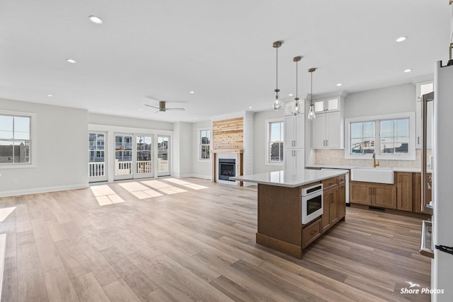 kitchen featuring a fireplace, light wood finished floors, light countertops, open floor plan, and a sink