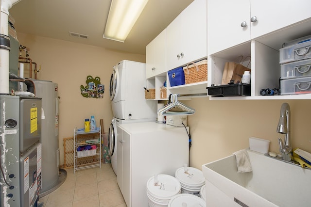 clothes washing area featuring sink, cabinets, water heater, light tile patterned flooring, and stacked washer and clothes dryer