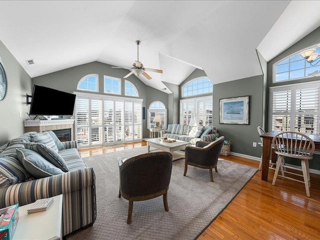 living room with a tiled fireplace, ceiling fan, a healthy amount of sunlight, and wood-type flooring