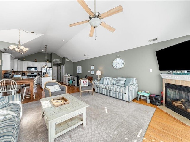 living room with a tiled fireplace, lofted ceiling, light hardwood / wood-style flooring, and ceiling fan with notable chandelier