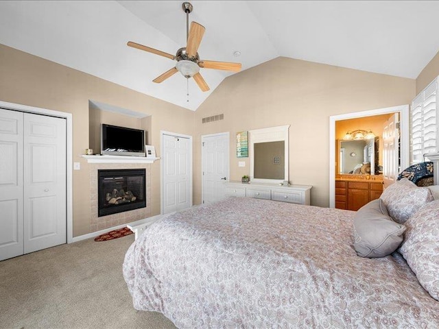 carpeted bedroom with a fireplace, two closets, vaulted ceiling, and ceiling fan