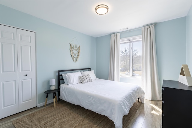 bedroom with wood finished floors, visible vents, a closet, and baseboards