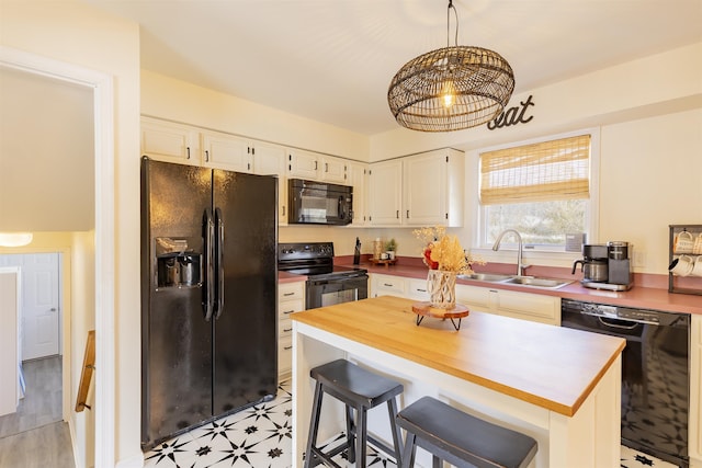 kitchen with black appliances, a sink, wood counters, white cabinets, and light floors