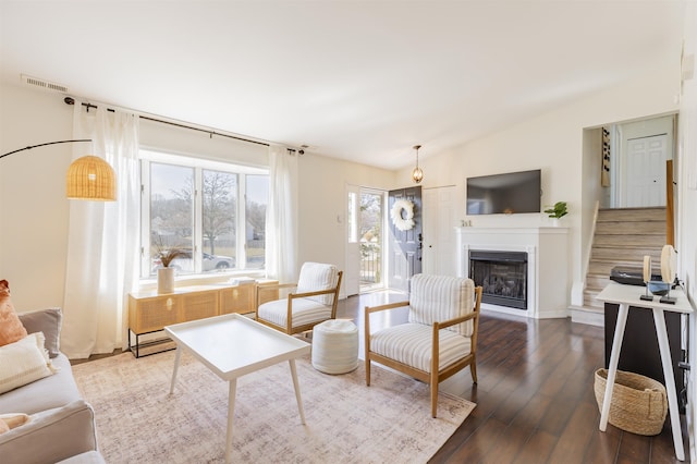 living area with visible vents, stairs, vaulted ceiling, a fireplace, and wood finished floors