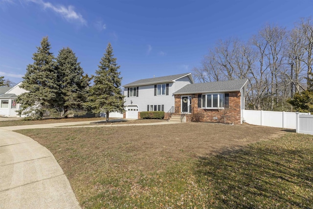 tri-level home featuring a front yard, fence, an attached garage, crawl space, and brick siding