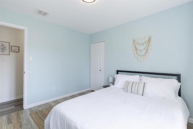 bedroom with a closet, visible vents, baseboards, and wood finished floors