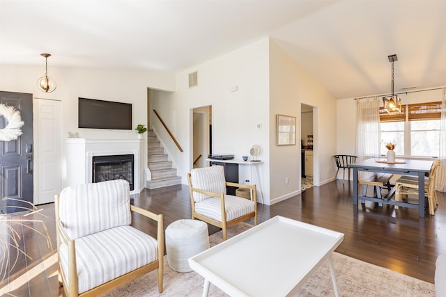 living room with a glass covered fireplace, lofted ceiling, wood finished floors, and visible vents