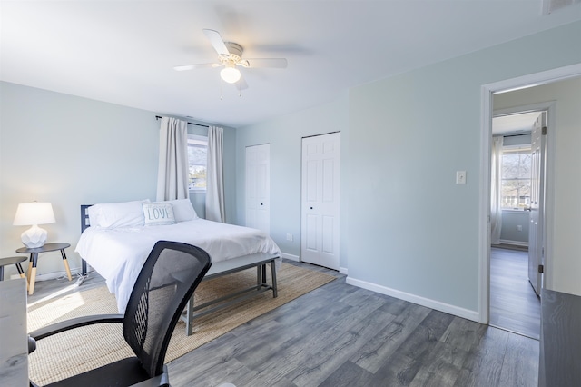 bedroom with visible vents, two closets, wood finished floors, baseboards, and ceiling fan