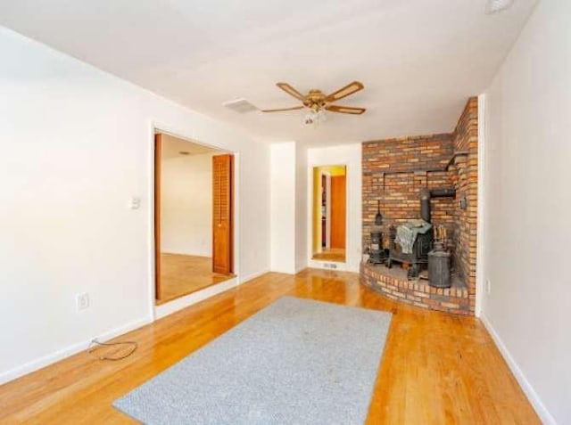 living room featuring ceiling fan, hardwood / wood-style floors, and a wood stove