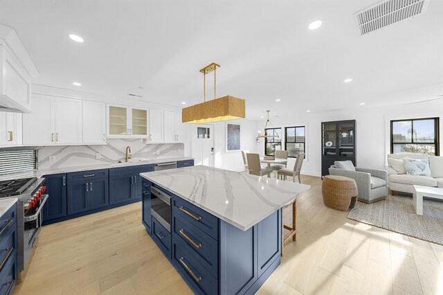 kitchen featuring decorative backsplash, stainless steel appliances, a kitchen island, pendant lighting, and white cabinetry