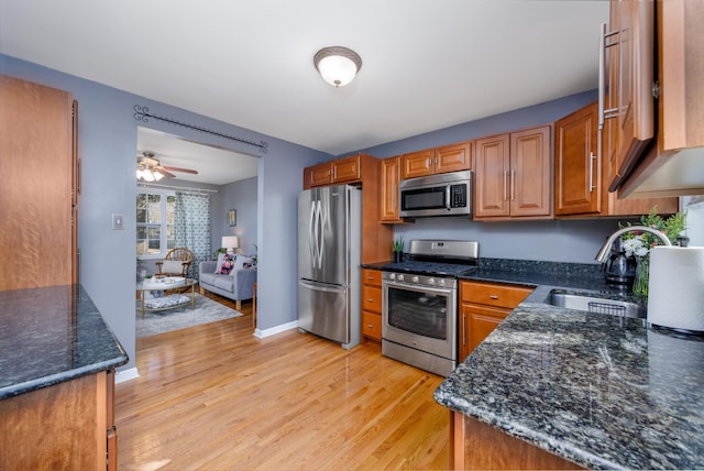 kitchen featuring sink, dark stone counters, light wood-type flooring, ceiling fan, and stainless steel appliances