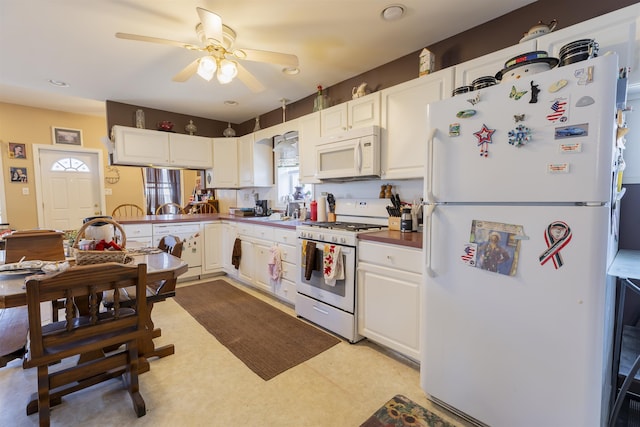 kitchen with white appliances, light floors, a peninsula, ceiling fan, and white cabinets