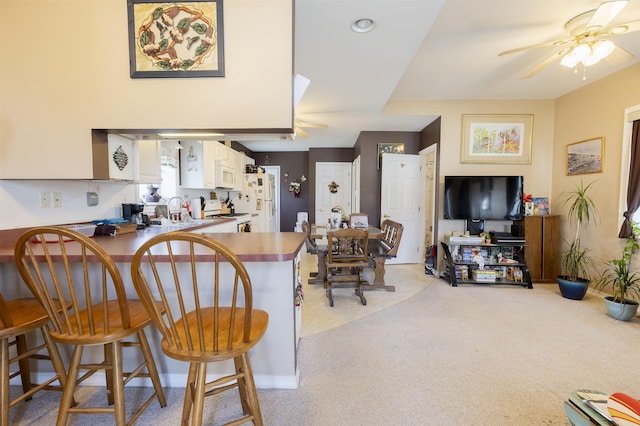 kitchen featuring light colored carpet, a kitchen breakfast bar, white appliances, a ceiling fan, and a sink