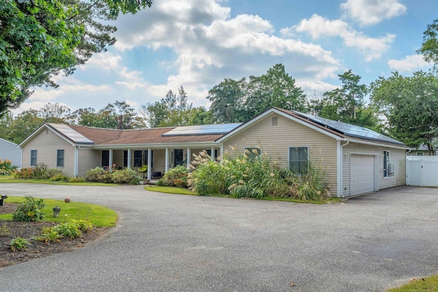 single story home with aphalt driveway, solar panels, a garage, and fence