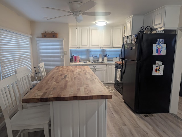 kitchen with sink, wooden counters, range, black refrigerator, and white cabinetry