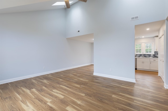 unfurnished living room featuring a skylight, high vaulted ceiling, and wood-type flooring