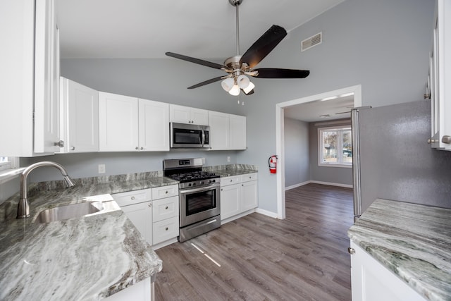 kitchen with visible vents, appliances with stainless steel finishes, light stone countertops, vaulted ceiling, and a sink