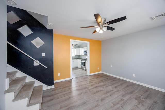 unfurnished living room with a ceiling fan, visible vents, baseboards, stairway, and light wood-type flooring