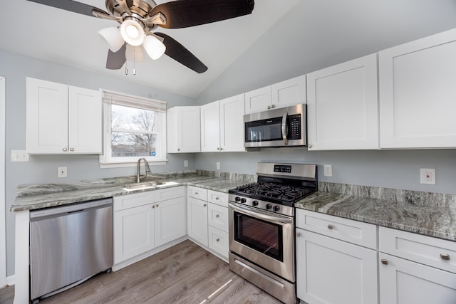 kitchen with appliances with stainless steel finishes, vaulted ceiling, white cabinetry, and a sink