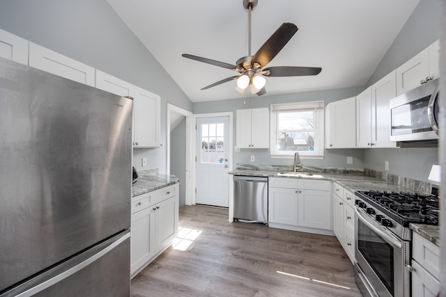 kitchen featuring vaulted ceiling, stainless steel appliances, light wood finished floors, and a sink