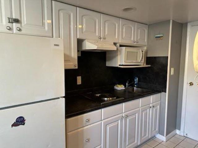 kitchen with light tile patterned flooring, range hood, white appliances, decorative backsplash, and white cabinets