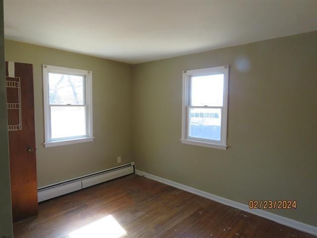 spare room featuring baseboard heating, wood finished floors, a wealth of natural light, and baseboards