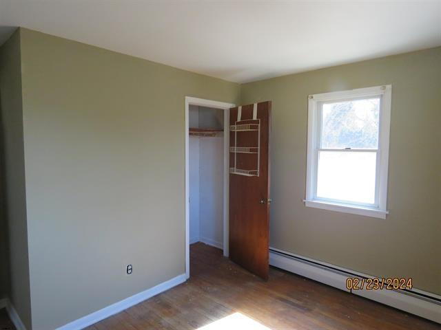 unfurnished bedroom featuring a baseboard radiator, a closet, baseboards, and wood finished floors