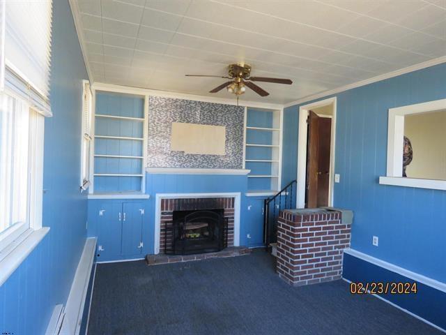 unfurnished living room featuring built in features, crown molding, a brick fireplace, carpet flooring, and ceiling fan