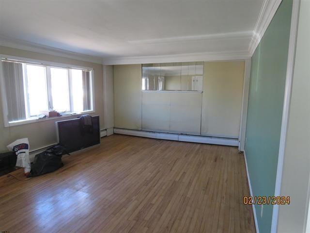 spare room with a baseboard radiator, crown molding, and wood finished floors