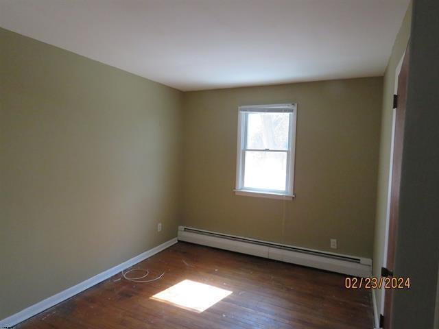 spare room featuring baseboards, a baseboard heating unit, and wood finished floors