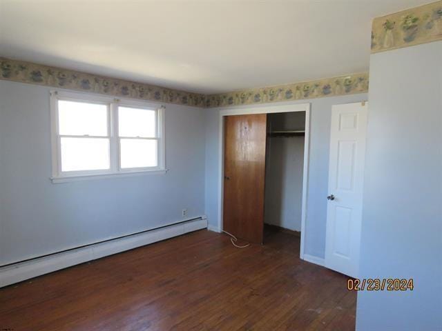 unfurnished bedroom featuring dark wood-style flooring, baseboard heating, a closet, and baseboards