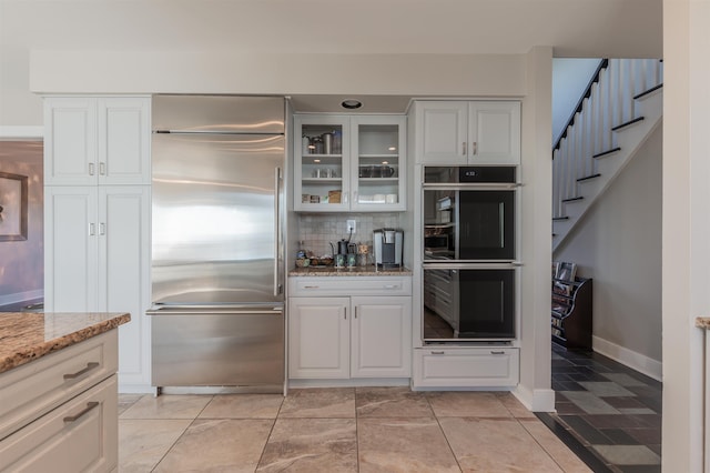 kitchen featuring built in fridge, light stone counters, white cabinetry, and double oven