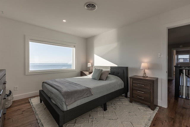 bedroom with hardwood / wood-style floors and a water view