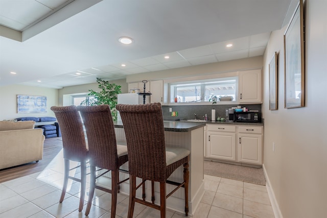 kitchen featuring a kitchen breakfast bar, tasteful backsplash, sink, light tile patterned floors, and white cabinetry